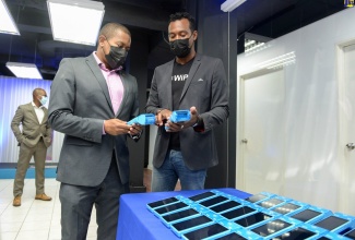 Minister of Agriculture and Fisheries, Hon. Floyd Green (left), speaking with WiPay’s Country Manager for Jamaica, Kibwe McGann, about the point-of-sale terminals that the organisation provides, during the opening ceremony for the entity’s WiPay’s headquarters in New Kingston on Thursday (August 26).