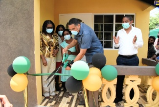 Prime Minister, the Most Hon. Andrew Holness  (second right), cuts the ribbon to officially hand over a three-bedroom house to a family in his West Central St. Andrew, recently. Others pictured (from left)) are Permanent Secretary in the Office of the Prime Minister, Audrey Sewell, family members for the unit, and Mayor of Kingston, Senator Delroy Williams.