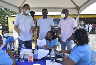 Prime Minister, the Most Hon. Andrew Holness (left, standing), engages with public health nurses, during a coronavirus (CoVID-19) vaccination blitz at the Pembroke Hall community centre in St. Andrew Northwest on Friday (September 24). He was accompanied by Minister of Finance and the Public Service and St. Andrew Northwest Member of Parliament, Dr. the Hon. Nigel Clarke (centre, standing); and Councillor for the Chancery Hall Division, Kingston and St. Andrew Municipal Corporation, Dwayne Smith. In the background is Commanding Officer for the Duhaney Park Police Station, Deputy Superintendent Coleridge Minto.


