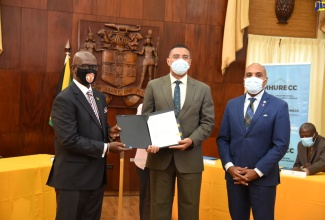 Prime Minister, the Most Hon. Andrew Holness (centre); and Minister of Local Government and Rural Development, Hon. Desmond McKenzie (left), display the signed Memorandum of Understanding (MOU) for the Victoria Palm housing development in Western Kingston, during the virtual launch ceremony on Friday (October 29). At right is Chief Executive Officer, Kingston and St. Andrew Municipal Corporation (KSAMC), Robert Hill.