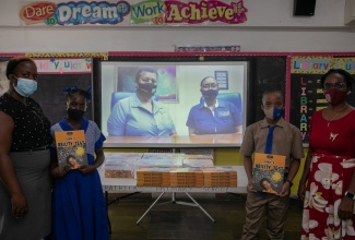 Students of the St. Patrick’s Primary School in Waterhouse, Kingston, Annastacia Williams (second left) and Shavaughn Bucchanan (second right), display the mental ability workbooks valued at $350,000, donated by Betting, Gaming and Lotteries Commission (BGLC) to aid in their Primary Exit Profile (PEP) preparations. Joining the students are Social Studies teacher, Jodian Walker (left)  and school Principal, Susan White. Representing the BGLC at the virtual handover ceremony are Manager for Corporate Affairs and Communication, Jeanette Lewis (on screen left), and Communications and Research Assistant, Tamara Myrie (on screen right).