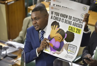 State Minister in the Ministry of Education, Youth and Information, Hon. Robert Morgan, shows a poster providing information about the 211 child abuse reporting hotline, which he requested Members of Parliament (MPs) to place in their constituency offices to aid in the fight against child abuse. The poster forms part of the information package on the hotline Mr. Morgan has put together for distribution by MPs to their constituents. Mr. Morgan was making his contribution to the 2021/22 State of the Constituency Debate during the sitting of the House of Representatives on Tuesday (October 12). 