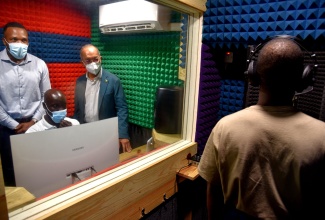 Minister of National Security, the Hon. Dr. Horace Chang (right), and reggae dancehall artiste Jeffrey ‘Agent Sasco’ Campbell, observes a recording session in the new Black Diamond Music Studio at the Metcalfe Street Secure Juvenile Remand Centre in Kingston, at the official opening ceremony of the facility on Wednesday (December 15). Seated at the computer is Acting Staff Officer for the We Transform programme, Department of Correctional Services (DCS) Meshach Brown.