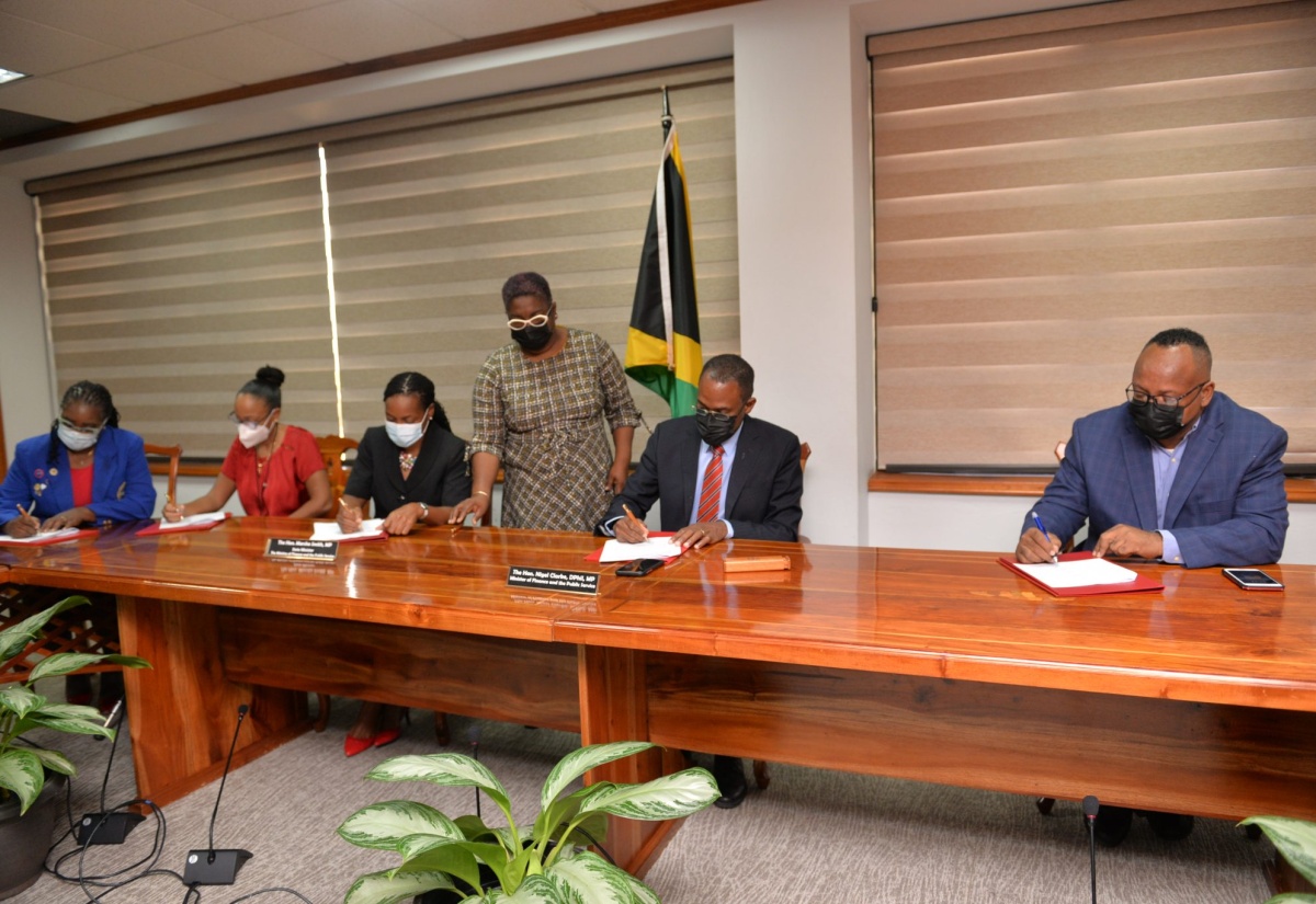 Minister of Finance and the Public Service, Dr. the Hon. Nigel Clarke (second right), and Minister of State, Hon. Marsha Smith (centre, seated), sign the Heads of Agreement formalising the Government’s four per cent wage increase offer for April 2021 to March 2022, with executives of three of the six additional unions/bargaining units representing public sector workers, which have accepted the provision. From left are: Nurses Association of Jamaica (NAJ) President, Patsy Henry; Jamaica Medical Doctors Association (JMDA) President, Dr. Mindi Fitz-Henley; and Union of Clerical, Administrative and Supervisory Employees (UCASE) General Secretary, John Levy. The signing was held at the Ministry in Kingston on Wednesday (December 22). Overseeing the proceedings is the Ministry’s Principal Director for Employee Relations, Lorna Phillips.

