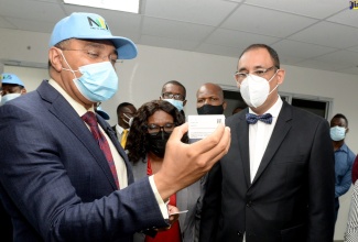 Prime Minister, the Most. Hon. Andrew Holness (left), displays a sample of the national identification system (NIDS) card, which was printed at the NIDS card centre at the Post and Telecommunication Department on South Camp Road in Kingston on January 4. Among those looking on are Permanent Secretary, Office of the Prime Minister, Audrey Sewell (centre), and Project Manager, PBS Consortium, Jorge Rueda (right).