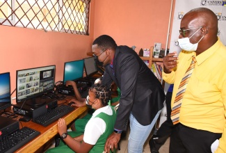 Minister of Information and Member of Parliament for Clarendon North Central, the Hon. Robert Morgan (centre), assists Grade six student, Anecia Simpson, in using a computer at the new Community Access Point (CAP) site, which opened at the Brixton Hill Primary and Infant School in the parish on Wednesday (January 19). Looking on, is Principal of the school, Leon Clare. The facility, established by the Universal Service Fund (USF), is equipped with 20 computers, a projector with accompanying screen and mount, and desks and chairs. It will provide residents, especially students, with access to Wi-Fi services to participate in online learning.