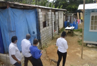 Minister of Local Government and Rural Development, Hon. Desmond McKenzie (second from left), visits the home of an indigent family in the Mint Road area of Grange Hill, Westmoreland. The family is to be assisted with housing under the Ministry’s indigent housing programme. 