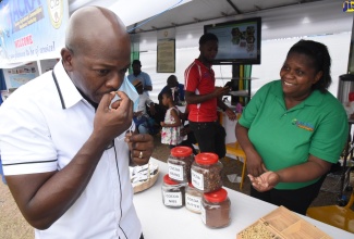 Agriculture and Fisheries Minister, Hon. Pearnel Charles Jnr, ‘smells the coffee’ while visiting the Jamaica Agricultural Commodities Regulatory Authority’s (JACRA) booth at AgroFest Jamaica on Saturday (May 28). The event was held at the Ministry’s Hope Gardens Complex in Kingston. At right is JACRA Administrator, Carline Wint-Mattison.