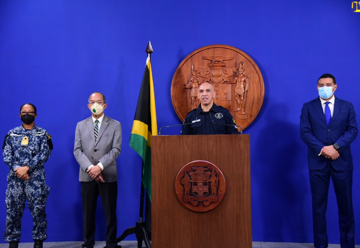 Prime Minister, the Most Hon. Andrew Holness (right), and Deputy Prime Minister and National Security Minister, Hon. Dr. Horace Chang  (second left), listen as Commissioner of Police, Major General Antony Anderson (at lectern), makes a statement during a virtual press conference held at the Office of the Prime Minister on Friday (June 17) at which a State of Public Emergency (SOE) was announced for the parish of St. Catherine. Also pictured is Chief of Defence Staff, Rear Admiral Antonette Wemyss-Gorman. 