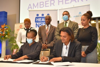 Prime Minister, the Most Hon. Andrew Holness (standing, second right), observes as Founder and Chief Executive Officer (CEO) of the Amber Group, Dushyant Savadia (seated right) and Managing Director (Acting), HEART/NSTA Trust, Novelette Denton Prince (seated left), sign the memorandum of understanding to formalise the partnership for the establishment of the Amber HEART Institute of Coding. Occasion was the graduation ceremony for the first cohort of trainees under the pilot Amber HEART Academy, at the AC Marriott by Kingston in St. Andrew on June 1. Others observing (from left, standing) are Deputy Managing Director (Acting), HEART/NSTA Trust, Kenesha Campbell; Chairman, HEART/NSTA Trust, Professor Alwin Wint; and Executive Assistant to the Founder and CEO, Amber Group, Juliana Moodie.