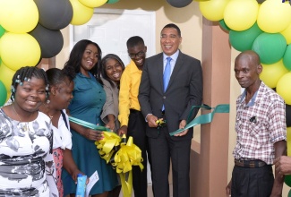 Prime Minister, the Most Hon. Andrew Holness (second right), cuts the ribbon to celebrate the official handover a new three-bedroom home to Delano Tucker (third right) and his family in Guy’s Hill, St. Catherine, on Wednesday (August 11). The unit was built under the New Social Housing Programme (NSHP). Joining in the occasion (from left) are daughter, Denisha Tucker; mother, Nattris Tucker; Member of Parliament for St. Catherine Northeast, Kerensia Morrison; Chairperson, Oversight Committee for NSHP, Judith Robb Walters, and father, Desmond Tucker.