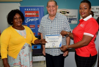 Minister of Transport and Mining, Hon. Audley Shaw, observes as participant in the Blue Ribbon First Responders Training, Carlene Barrett (left), receives her certificate from Chief Operating Officer at British Caribbean Insurance Company, Michelle Anderson. The presentation ceremony was held at the University of Technology, Jamaica, on Thursday, August 11 