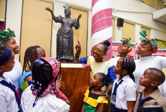 Culture, Gender, Entertainment and Sport Minister, Hon. Olivia Grange (third right, back row), admires a statuette depicting late cultural icon, Dr. the Hon. Louise “Miss Lou” Bennett-Coverley, which was unveiled during a ceremony at the University of the West Indies (UWI), Mona, Library, in St. Andrew, on Wednesday (September 7). The unveiling formed part of the opening of the Miss Lou Exhibition, which is among several activities commemorating the 103rd anniversary of the beloved cultural exponent’s birth. With Ms. Grange are students and members of several award-winning groups, who performed in the Jamaica Cultural Development Commission (JCDC) 2022 National Festival of the Performing Arts. 