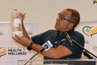 Minister of Health and Wellness, Dr. the Hon. Christopher Tufton, gives a visual display of the sugar content in a bottle of sugar-sweetened beverage during a recent press briefing at the Jamaica Pegasus Hotel in New Kingston.