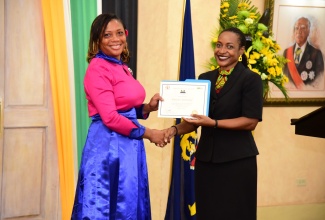 Minister of State in the Ministry of Finance and the Public Service, Hon. Marsha Smith (right), presents the 2022 Marcus Garvey Public Graduate Scholarship to Constable Simone Murray of the Jamaica Constabulary Force, during the awards ceremony at King’s House in August.

