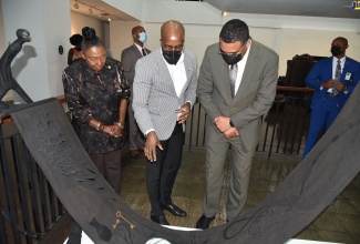 Prime Minister, the Most Hon. Andrew Holness (right) and Minister of Culture, Gender, Entertainment and Sport, Hon. Olivia Grange (left) listen as Chief Curator at the National Gallery of Jamaica (NGJ), O’Neil Lawrence, highlights the elements of a work of art, during a recent tour of the ‘Kingston Biennial 2022: Pressure,’ exhibition at the NGJ in downtown Kingston.  The occasion was a ceremony held at the National Gallery to hand over the late David Boxer’s art collection to the NGJ and the new Houses of Parliament.