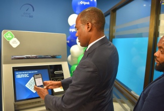 Minister of Finance and the Public Service, Dr. Hon. Nigel Clarke (left),  uses the LYNK Automated Banking Machine (ABM) Cash in and Cash out feature during the media launch at the Atrium, National Commercial Bank (NCB), New Kingston on September 20. Looking on is Chief Executive Officer of LYNK, Vernon James.