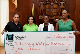 Member of Parliament, St. Andrew East Rural, the Most Hon. Juliet Holness (right), and Managing Director, V. Mansuhkani Foundation,  Gul Mansuhkani (left), present a symbolic cheque for scholarships, valued $2 million, to University of the West Indies (UWI) students, Gavieal Gordon (second right) and Zoe Hitchins. The presentation took place at Jamaica House on Thursday (September 15). 