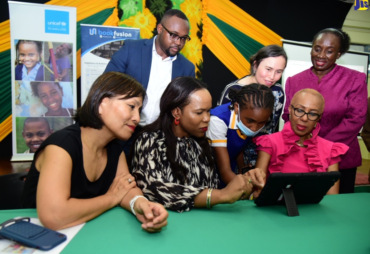 Minister of Education and Youth, Hon. Fayval Williams (seated, right) along with (seated from left) United Nations Children’s Fund (UNICEF) Jamaica Country Representative, Mariko Kagoshima; Acting Chief Education Officer in the Ministry of Education and Youth, Dr. Kasan Troupe and grade-seven student at St. Hugh’s High School, Shakacia Greenland, view a digital textbook, at the recent launch of the Accessible Digital Textbook Prototype in Jamaica at the Joyce Robinson Hall, Kingston and St. Andrew Parish Library. Others (standing from left) are Founder and Chief Executive Officer, BookFusion, Dwayne Campbell; Regional Inclusive Education and Disability Specialist, UNICEF, Cynthia Brizuela and Director General, Jamaica Library Service, Maureen Thompson.