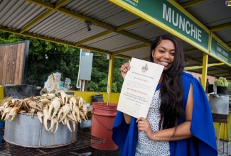 Recent graduate from the University of the West Indies (UWI), Mona, Alexia Hibbert, displays her Bachelor of Science Degree with Honours certificate while standing beside the crab cooking station in Kingston where her mother, Makeisha “Munchie” Walker, works. She now holds a major in Political Leadership, Strategy and Management and a minor in Political Science. Ms. Hibbert visited her mother on Tuesday (November 1), to share her award with Ms. Walker and express gratitude for funding her tertiary education.