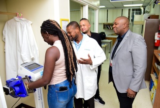 Geophysics student,  University of the West Indies (UWI), Naima Snaggs (left), demonstrates the use of a Berthold hand-foot radiation contamination monitor with the assistance of Head of the Nuclear Analytical Laboratory at the International Centre for Environmental and Nuclear Sciences (ICENS), Johann Antoine (second left). Looking on are Chairman of ICENS, Dr. Parris Lyew-Ayee Jr (second right); and Director General, ICENS and Professor of Applied Nuclear Sciences, Professor Charles Grant. The event was the ICENS open day and media tour of the facility located on the UWI’s Mona Campus on Tuesday, November 29. 