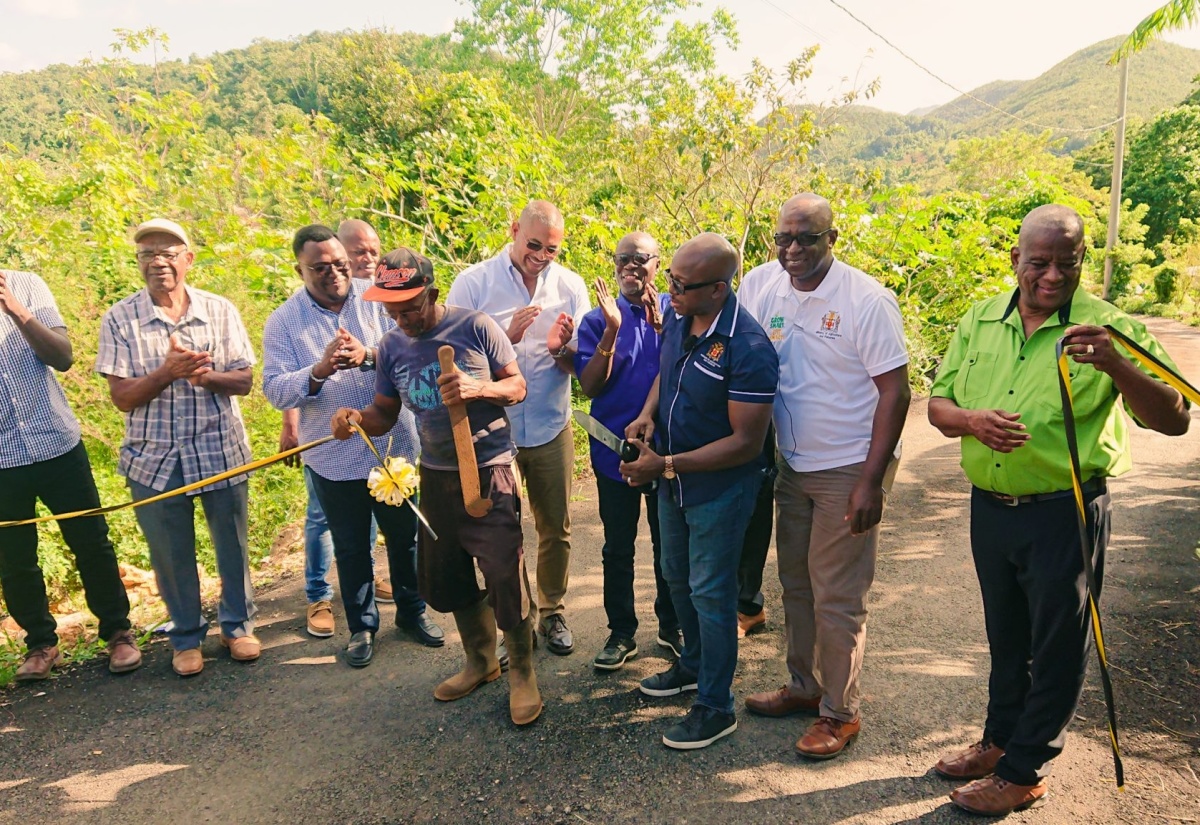 Minister of Agriculture and Fisheries, Hon. Pearnel Charles Jr. (third right), is assisted by Maidstone farmer Silburn Steadman (with machete) in cutting the ribbon to officially open the Grass Piece farm road in Manchester on Thursday (December 15). Among the other participants are Minister of State in the Ministry of Agriculture and Fisheries, Hon. Franklyn Witter (right); Member of Parliament, Manchester North Western, Mikael Phillips (fifth right), as well as representatives of the Rural Agricultural Development Authority (RADA). 