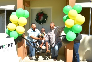 Prime Minister, the Most Hon. Andrew Holness (left) and Member of Parliament, Manchester North Western, Mikael Phillips, assist beneficiary of the Government’s New Social Housing Programme (NSHP), 69-year-old Tesselyn Roach, to cut the ribbon to her new three-bedroom home in Free Town district on Friday (Dec. 16). Ms. Roach lost her house to fire, which also claimed the life of her two-year-old granddaughter, four years ago. She stayed with her cousin, who also lives in the community, prior to receiving her new home. 