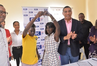 Prime Minister, the Most Hon. Andrew Holness (third right), applauds as new beneficiary, Sidonie Eldemire (fourth right), and son Rohan Clarke (fourth left), display the keys to their home, which they received under the New Social Housing Programme. The unit was constructed and donated by Arc Properties Limited.  Looking on (from left) are Arc Properties Chairman, Norman Horne, General Manager, Ashley-Ann Foster Horne, and Deputy Chairperson, Charlotte Hayles; Chief Executive Officer, Kinetic Engineering Services Limited, Keon Hinds, and Permanent Secretary in the Office of the Prime Minister and the Ministry of Economic Growth and Job Creation, Audrey Sewell. The presentation was made on Wednesday, (December 14). 