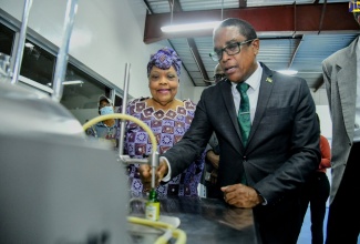 State Minister in the Ministry of Industry, Investment and Commerce, Dr. the Hon. Norman Dunn (right), observes the process for manufacturing essential oils at the Jamaica Business Development Corporation (JBDC) incubator in Kingston, following the facility’s recent commissioning.  Looking on is JBDC Chief Executive Officer, Valerie Veira.