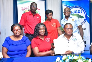 Minister of Agriculture and Fisheries, Hon. Pearnel Charles Jr. (standing, right,) looks on as Chief Executive Officer of Home Grown Produce, David Young (seated, right) and Cascade Community Farmers Group member, Thelma Watson (seated, centre), display a signed contract, during an Agri-Business Symposium on January 19 at the Tropics View Hotel in Manchester. Others sharing the moment (from left) are Davis Town Farmers Group member, Juliet Taylor;  Rural Agricultural Development Authority (RADA) Manchester Parish Manager, Winston Miller; and  Angella Walker from the Cascade Community Farmers Group.

