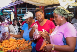 Minister of State in the Ministry of Health and Wellness, Hon. Juliet Cuthbert-Flynn (second right) makes a purchase from Tanya Bentley inside the Morant Bay Market, during a Pop-Up held by the Ministry and the Rural Agricultural Development Authority (RADA) on February 10.