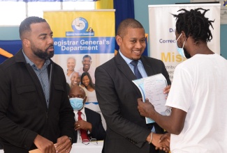 Minister Without Portfolio in the Office of the Prime Minister, Hon. Floyd Green (centre), hands over a free birth certificate under the ‘Operation Birthright’ project to an inmate of the St. Catherine Adult Correctional Centre, at the facility in Spanish Town, on Wednesday (February 15). Looking on is Chief Executive Officer and Deputy Keeper of Records, Registrar General’s Department (RGD), Charlton McFarlane.