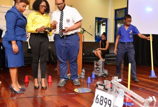 Acting Assistant Chief Education Officer in the Ministry of Education and Youth, Sophia Forbes Hall (left), looks on in amazement as Chief Executive Officer of the NCB Foundation, Nadeen Matthews Blair (centre), operates a robot built by the Jamaica College (JC) robotics team. Member of the  JC team, Michael Woods, provides instructions on how to operate the robot.  Occasion was Wednesday’s (February 15) launch of the NCB Foundation’s National Robotics Championship at the NCB Wellness and Recreation Centre in St. Andrew.  The competition will be held at the JC Auditorium from February 24 to 25.