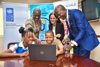 Grade-six students at Constant Spring Primary School in St. Andrew, Romiah Jule (left, seated) and Stephen Dennis (right, seated) are assisted by (from left) United Nations Development Programme (UNDP) Resident Representative, Denise Antonio; Deputy Regional Director, UNDP Latin America and the Caribbean, Linda Maguire; and Chief Executive Officer, Universal Service Fund (USF), Daniel Dawes, to navigate a computer software. The event was the closing ceremony for the Advancing Jamaica’s Digital Response to COVID-19 Rapid Finance Facility (COVID-RFF) Project on Wednesday (April 19), at the UNDP’s Kingston office. 