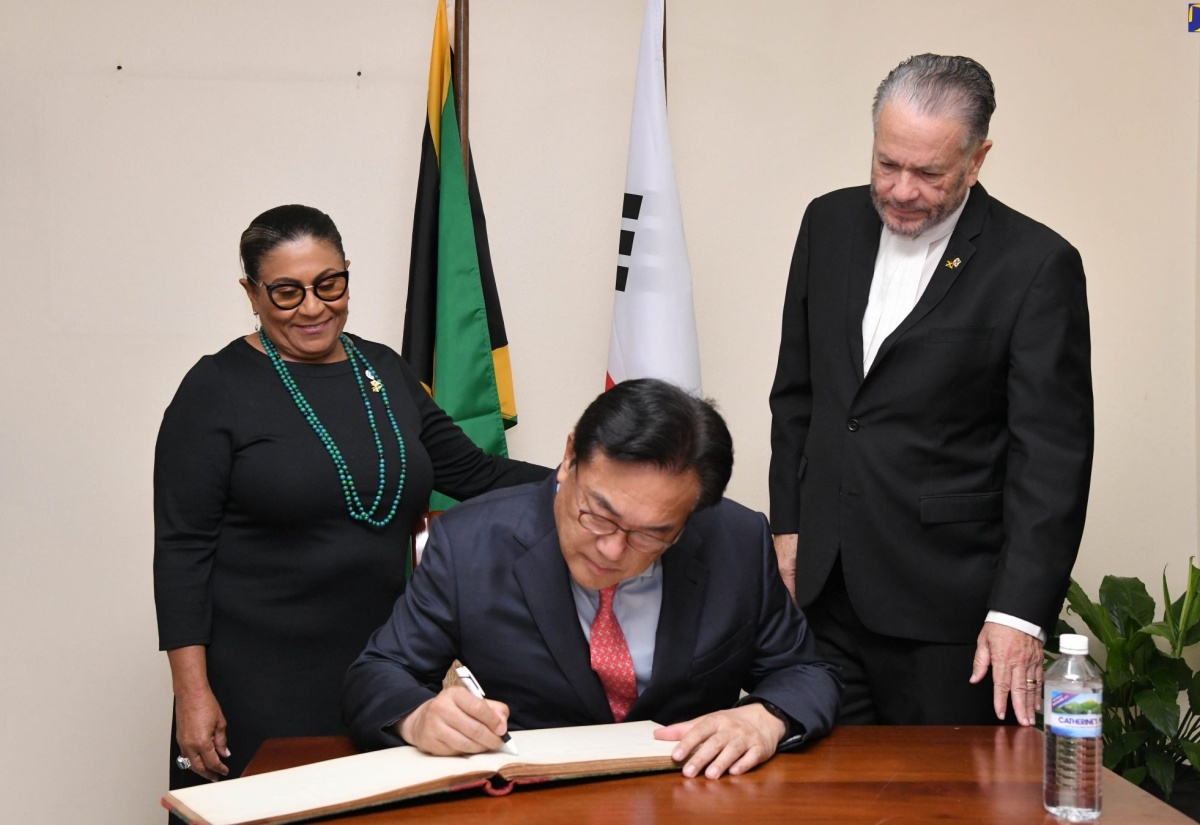 Speaker of the House of Representatives, Marisa Dalrymple-Philibert (left) and President of the Senate, Senator the Hon. Thomas Tavares-Finson (right) look on as President of the Korea-Jamaica Parliamentary Friendship Group, Chung Jin-suk, signs the guest book during the visit to Gordon House on April 19.