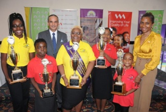 The five age group champions of the 2022 National Reading Competition (foreground, from left): Janae Brown (12-14) who represented the St. Ann Parish Library Network; Allyiauna Gordon (15-20) from the St. Thomas Parish Library Network; Adlyn Smith Graham (21 and over) from the Kingston and St. Andrew Parish Library Network; Aly-Anna Holness (nine-11) from the St. Catherine Parish Library Network, and Cavane Carter (six-eight) from the Portland Parish Library Network. Celebrating with them are (background, from left) JLS Board Chairman, Paul Lalor, and Chief Executive Officer, VM Foundation, Samantha Charles. The 2021 and 2022 National Champions were awarded during a ceremony at The Jamaica Pegasus hotel last August.