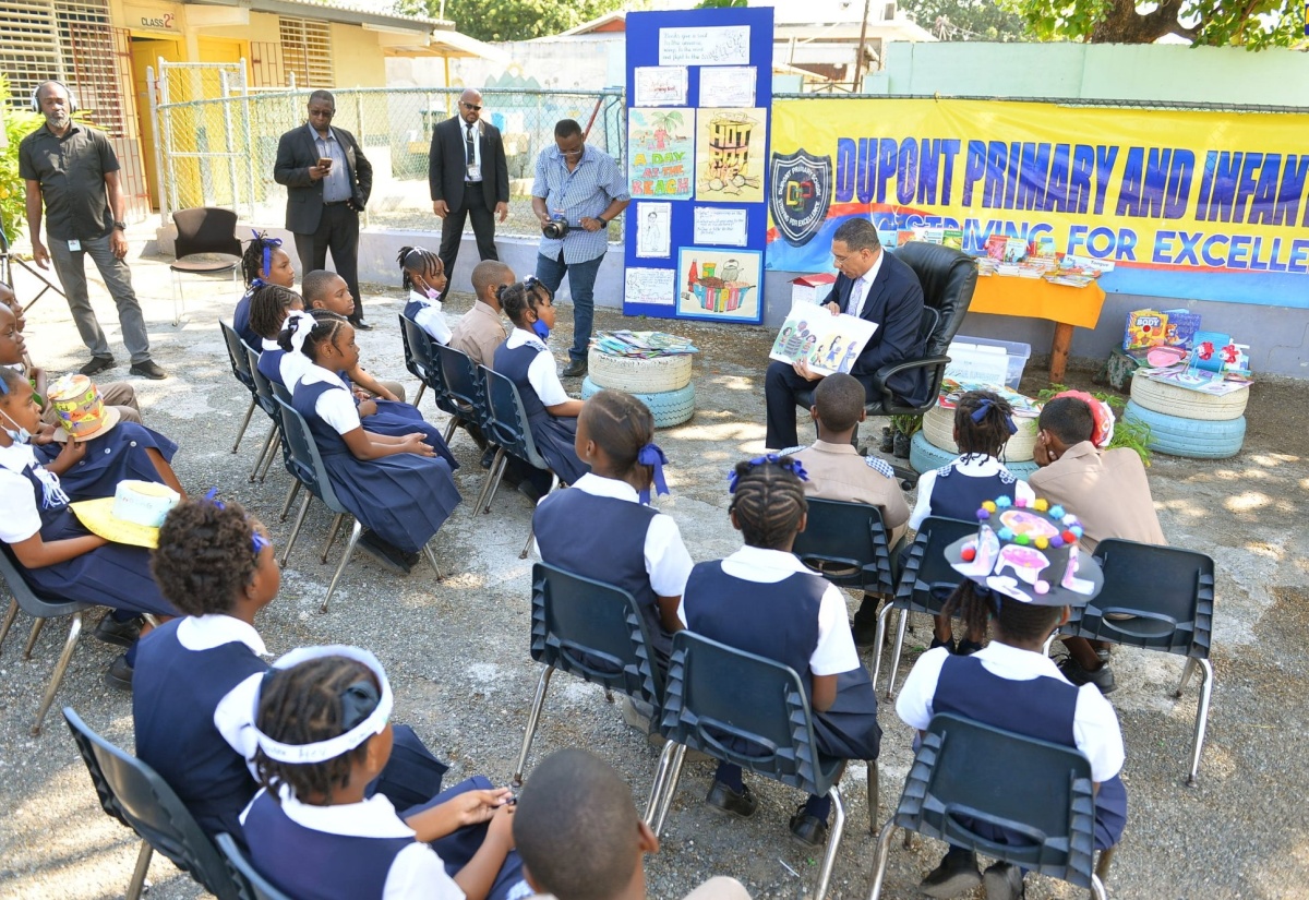 Prime Minister, the Most Hon. Andrew Holness (right, seated), points to illustrations in the book ‘I Can Do My Part’, by Cathryn O’Sullivan, while reading to grade-four students at Dupont Primary and Infant School. The occasion was a visit to the institution, located in his St. Andrew West Central constituency, as part of activities marking Read Across Jamaica Day on Tuesday (May 9).  