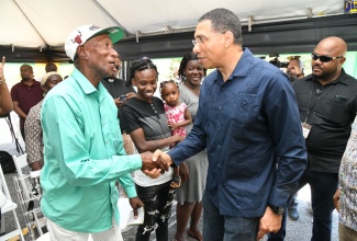 Prime Minister, the Most Hon. Andrew Holness (second right), greets Lloyd White, beneficiary under the New Social Housing Programme, during the official handover of three housing units at Goodwin Park Road in Central Kingston, on April 28. The other beneficiaries (from second left) are Leisha Brown, who is holding her baby, Mishka; and Lesa Brown.