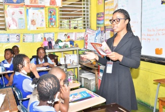 Manager of the Jamaica Information Service (JIS) Montego Bay Regional Office, Tashion Hewitt Stennett, reads to attentive grade three students of the Catherine Hall Primary and Infant School in St. James, during Read Across Jamaica Day activities at the institution on Tuesday ( May 9).