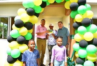 Prime Minister, the Most Hon. Andrew Holness (left), presents the key to Roger Mitchell (centre), a recipient of a three-bedroom unit under the New Social Housing Programme (NSHP), in Straun Castle, Manchester, recently. Sharing in the occasion are Transport and Mining Minister, and Member of Parliament for Manchester North East, Hon. Audley Shaw (right), and (foreground) family members of the new homeowner, Roger Mitchell Jr. and Brianna Mitchell.