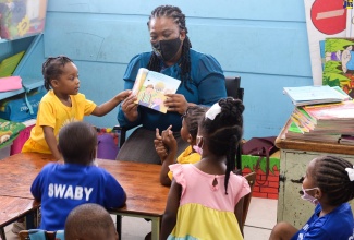 Students at the Webster Memorial Basic School are engaged in a reading session led by Audit Manager at the National Solid Waste Management Authority (NSWMA), Karen Watson. The session formed part of Read Across Jamaica Day activities across the island on May 9.