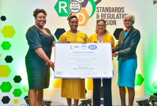 Minister of State in the Ministry of National Security, Hon. Juliet Cuthbert Flynn (second left), who is the former State Minister of Health and Wellness, joins Chief Medical Officer, Dr. Jacquiline Bisasor-McKenzie (second right) and Director of the Standards and Regulations Division in the Ministry of Health and Wellness, Cynthia Lewis Graham (right), in displaying the symbolic International Organization for Standardisation (ISO) 9001:2015 Certificate, which was handed over to the Ministry of Health during a recent ceremony at The Jamaica Pegasus hotel in New Kingston. Making the presentation is Manager of the National Certification Body of Jamaica (NCBJ,  Navenia Wellington Ford.
The Standards and Regulation Division (SRD) of the Ministry of Health and Wellness having earned ISO certification marks a shift in its level of operational efficiency and the quality of its service delivery to the public.

