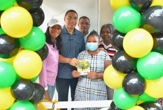 Prime Minister, the Most Hon. Andrew Holness (second left), makes a presentation to Blenheim, Manchester resident, Carla Pinnock, who is the recipient of a two-bedroom home, built in the community under the New Social Housing Programme (NSHP). Prime Minister Holness presented Ms. Pinnock with the keys on Friday (July 14). Sharing the occasion are (from left) Members of Parliament for Manchester Central, Rhoda Moy Crawford, and Manchester Southern, Robert Chin; and Principal Finance Officer, Ministry of Economic Growth and Job Creation, Judith Robb-Walters, who chairs the NSHP Oversight Committee