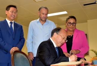President of the Senate, Hon. Thomas Tavares-Finson (centre); Speaker of the House of Representatives, Hon. Marisa Dalrymple-Philibert (right), and Ambassador of the People’s Republic of China to Jamaica, His Excellency Chen Daojiang (left), observe as Deputy to the National People’s Congress, Chairman of the Standing Committee of Beijing Municipal People’s Congress (BMPC), Li Xiuling (seated), signs the guest book during his courtesy call at the Ministry of Foreign Affairs and Foreign Trade in downtown Kingston on Thursday (September 14).

