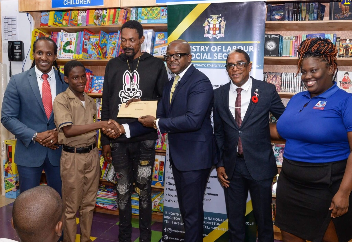 Minister of Labour and Social Security, Hon. Pearnel Charles Jr. (third right), presents a gift certificate to Bobby Carson Jr. (second left) during a presentation ceremony held for residents of Gregory Park, St. Catherine, who were affected by a firebombing incident earlier this year. The ceremony was held at the Kingston Bookshop, Portmore Town Centre, St. Catherine, on Thursday (October 5). Others (from left) are State Minister in the Ministry of Foreign Affairs and Foreign Trade and Member of Parliament for St. Catherine East Central, Hon. Alando Terrelonge; Bobby Carson Sr.; State Minister in the Ministry of Labour and Social Security, Dr. the Hon. Norman Dunn, and Supervisor, Kingston Bookshop, Portmore, Karaoke Harrison. The gift certificates, valued $15,000.00 each, are redeemable at Kingston Bookshop branches islandwide.