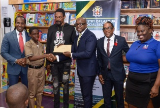 Minister of Labour and Social Security, Hon. Pearnel Charles Jr. (third right), presents a gift certificate to Bobby Carson Jr. (second left) during a presentation ceremony held for residents of Gregory Park, St. Catherine, who were affected by a firebombing incident earlier this year. The ceremony was held at the Kingston Bookshop, Portmore Town Centre, St. Catherine, on Thursday (October 5). Others (from left) are State Minister in the Ministry of Foreign Affairs and Foreign Trade and Member of Parliament for St. Catherine East Central, Hon. Alando Terrelonge; Bobby Carson Sr.; State Minister in the Ministry of Labour and Social Security, Dr. the Hon. Norman Dunn, and Supervisor, Kingston Bookshop, Portmore, Karaoke Harrison. The gift certificates, valued $15,000.00 each, are redeemable at Kingston Bookshop branches islandwide.