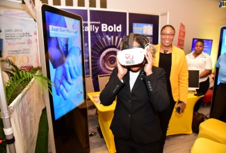 Minister without Portfolio in the Office of the Prime Minister with Responsibility for Skills and Digital Transformation, Senator Dr. the Hon. Dana Morris Dixon (foreground), immerses in the world of virtual reality while participating in today’s (November 29) second annual Government of Jamaica (GOJ) Technology Showcase at the AC Hotel in New Kingston. Behind the Minister is Acting Chief Executive Officer of eGov Jamaica Limited, Anika Shuttleworth.