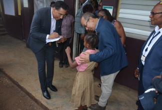 Prime Minister, the Most Hon. Andrew Holness (left), writes his signature for young Lizzmoy Dingwall of Chetwood Memorial Primary and Infant School in St. James, during a visit to the institution on Thursday (November 9.). Sharing in the moment is Deputy Prime Minister and Minister of National Security, Hon. Dr. Horace Chang. The Prime Minster paid condolences to the school community following the death of two of its students – seven-year-old Justin Perry and nine-year-old Nahcoliva – when the taxi in which they were travelling was shot up by gunmen in Salt Spring on Monday (November 6).

