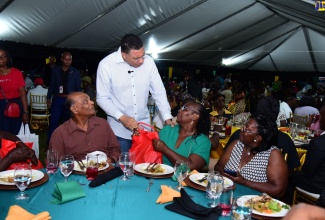 Prime Minister, the Most Hon. Andrew Holness (second left), presents a gift package to a senior citizen, at the Office of the Prime Minister (OPM) end-of-year senior citizens treat. The event was held on the lawns of Jamaica House on Saturday (December 16).