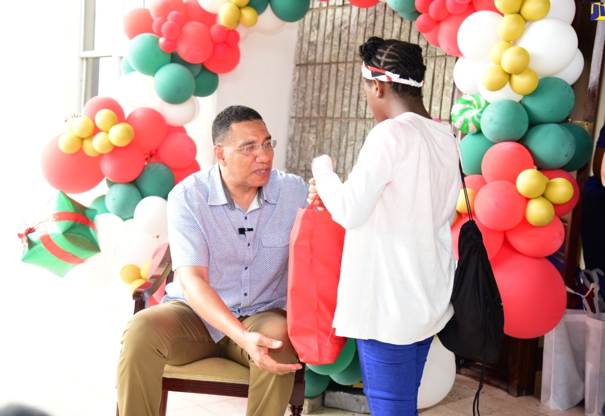 Prime Minister, the Most. Hon. Andrew Holness (left) presents Christmas gifts to a child in State care, during his annual treat for children, which was held on the grounds of the Office of the Prime Minister on Sunday (December 17).